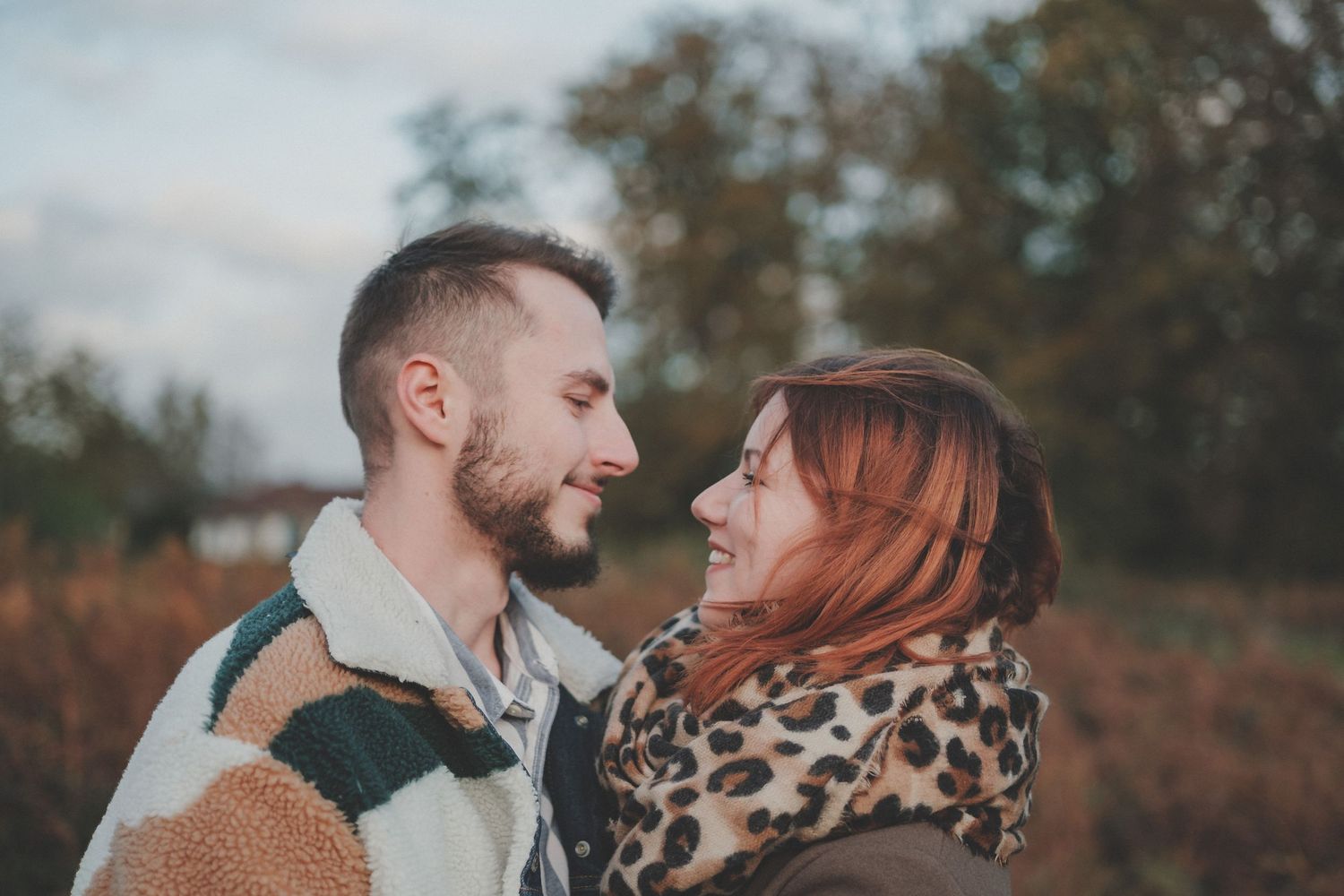 A couple in cozy autumn attire shares an intimate moment against a fall landscape.