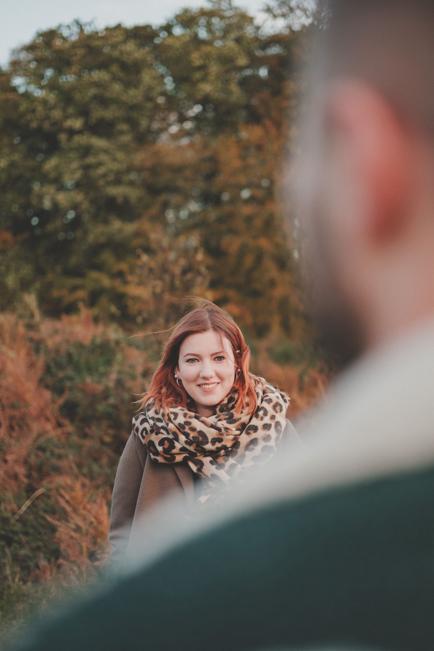 A candid autumn portrait featuring someone wearing a leopard print scarf among fall foliage.