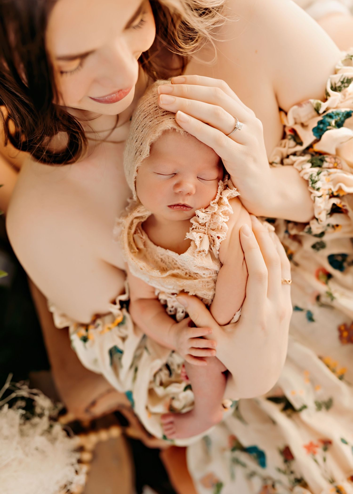 A tender moment between a mother and newborn baby dressed in lace against a floral backdrop.