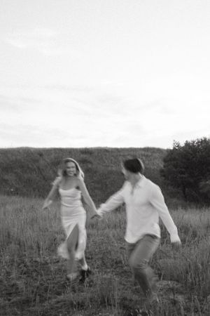 Joyful couple running through field at sunset in black and white.