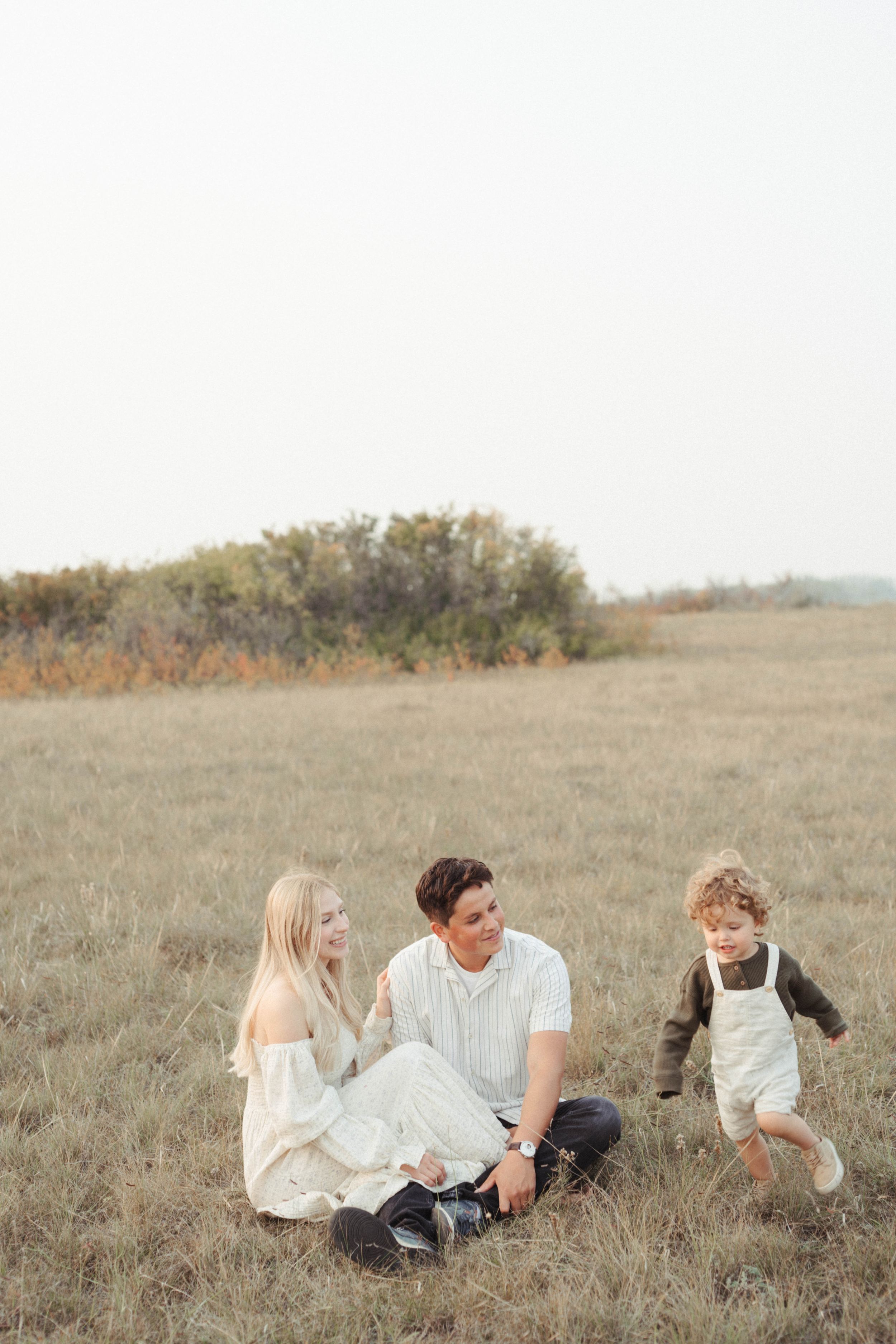 Family sits together in golden field during sunset photoshoot.