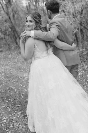 A romantic wedding couple embraces outdoors in a natural setting captured in black and white photography.