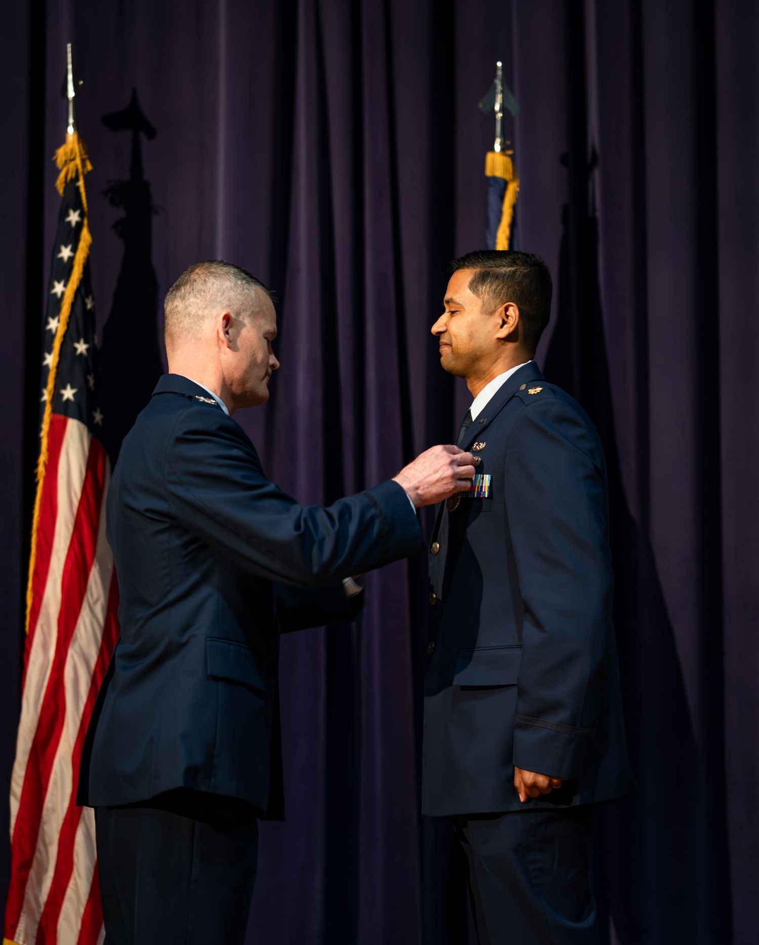 A military ceremony showing the pinning of medals between two service members in dress uniforms.