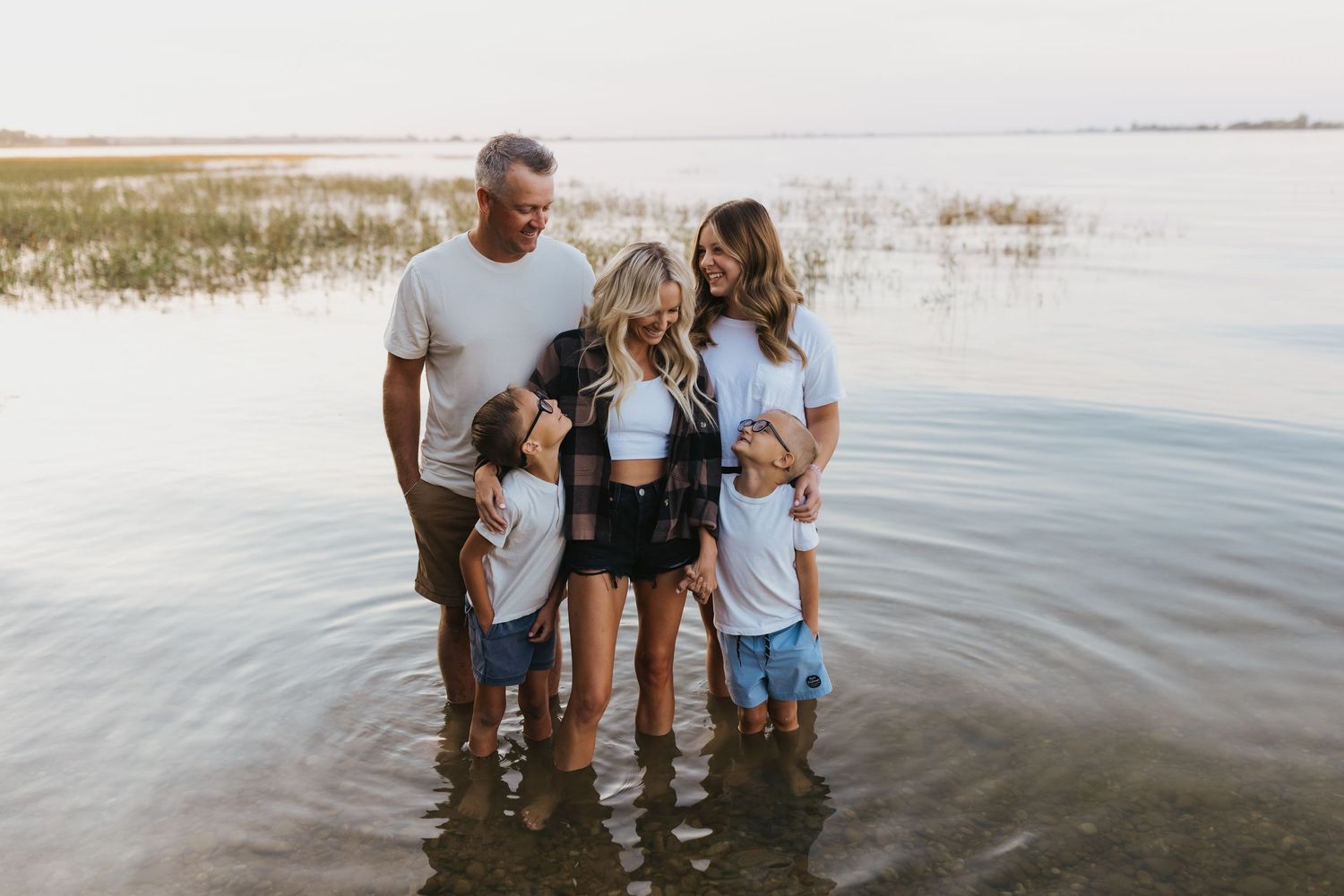 A family stands together in shallow water at the beach during sunset.