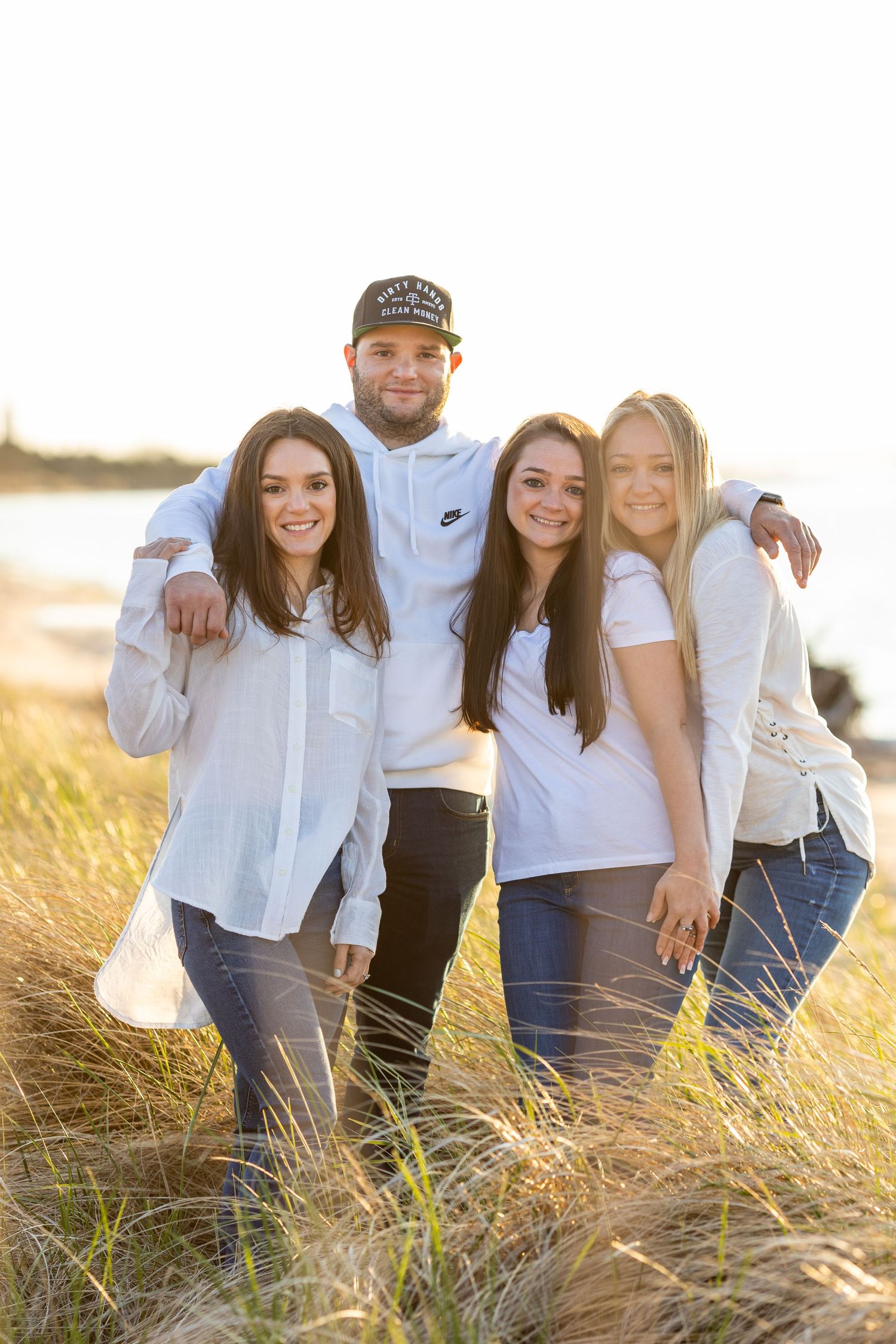 Group in coordinated white outfits poses together in golden sunset field.