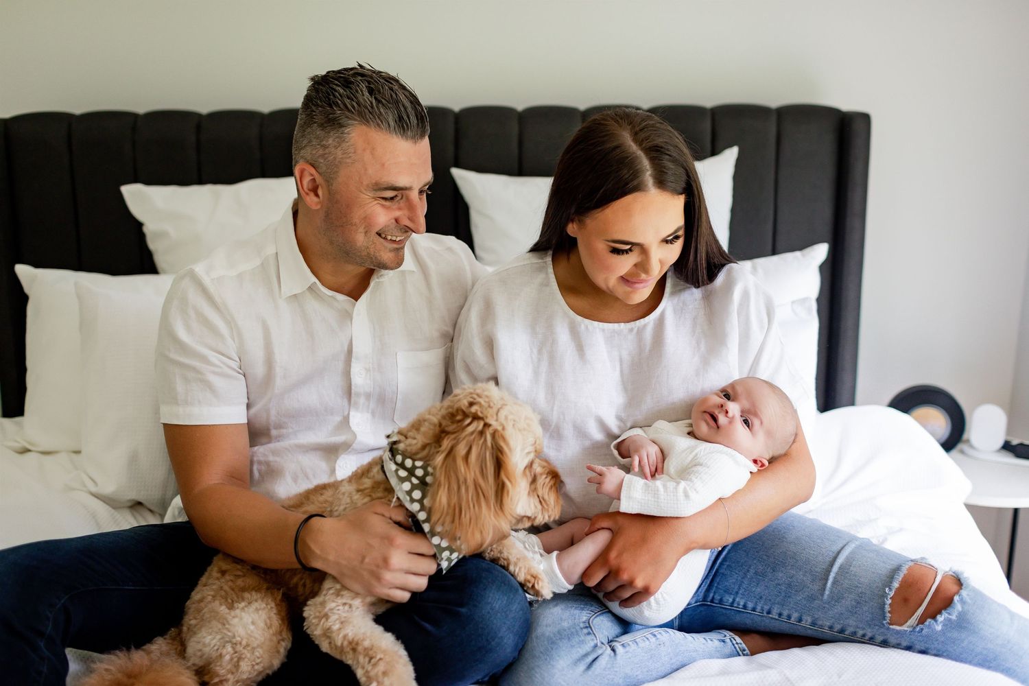 Family relaxing together on bed with their furry dog and newborn baby.