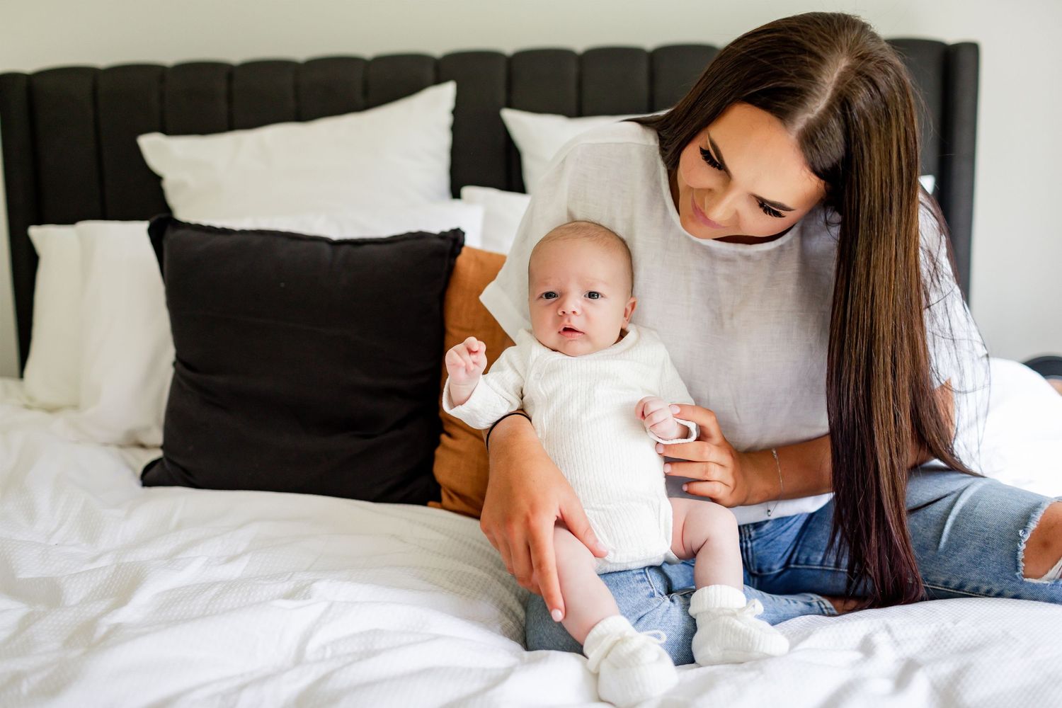 Mother and baby in white outfits share special moment on bed.