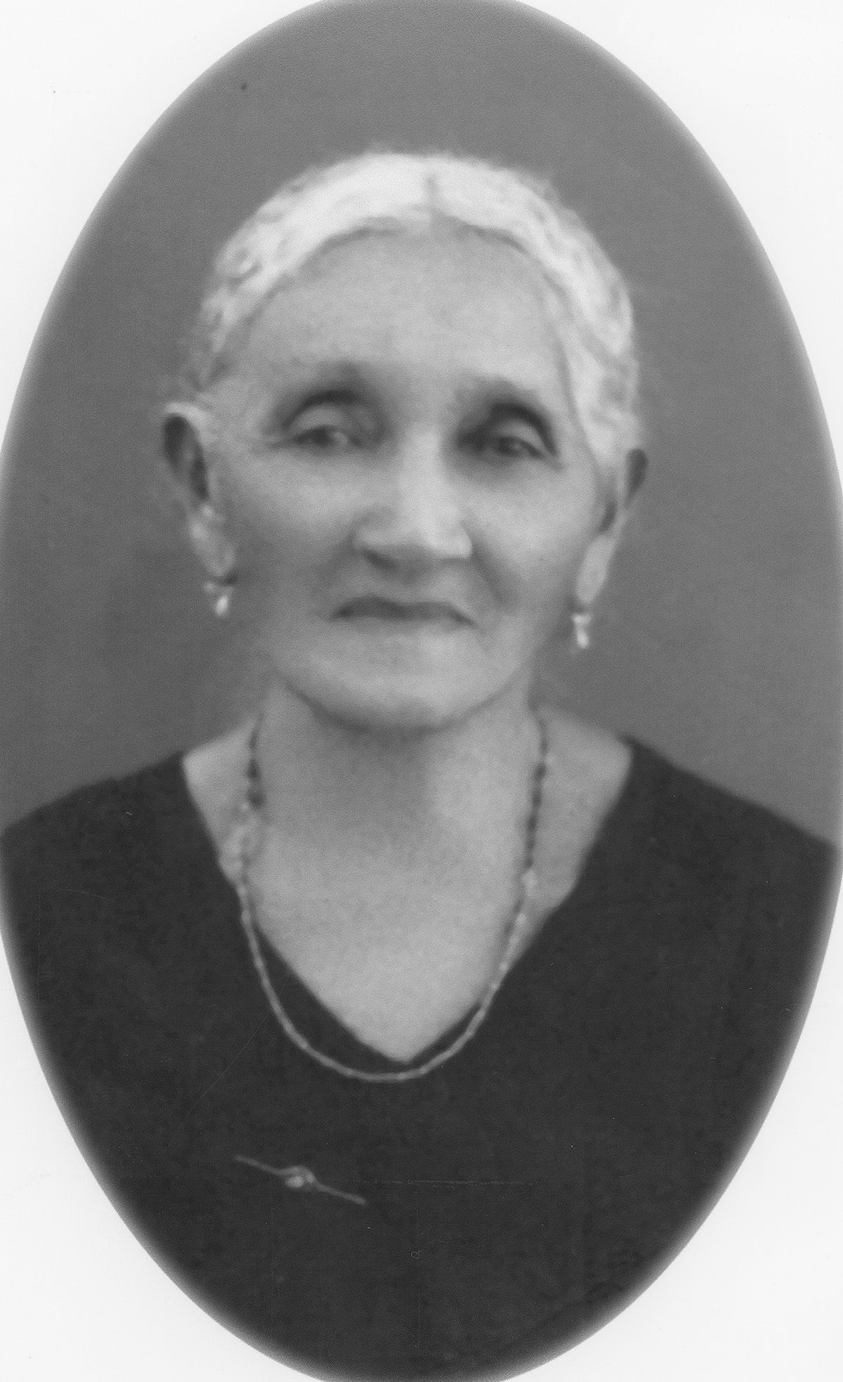 An oval-framed vintage black and white portrait photograph of an elderly person wearing a necklace and dark dress.