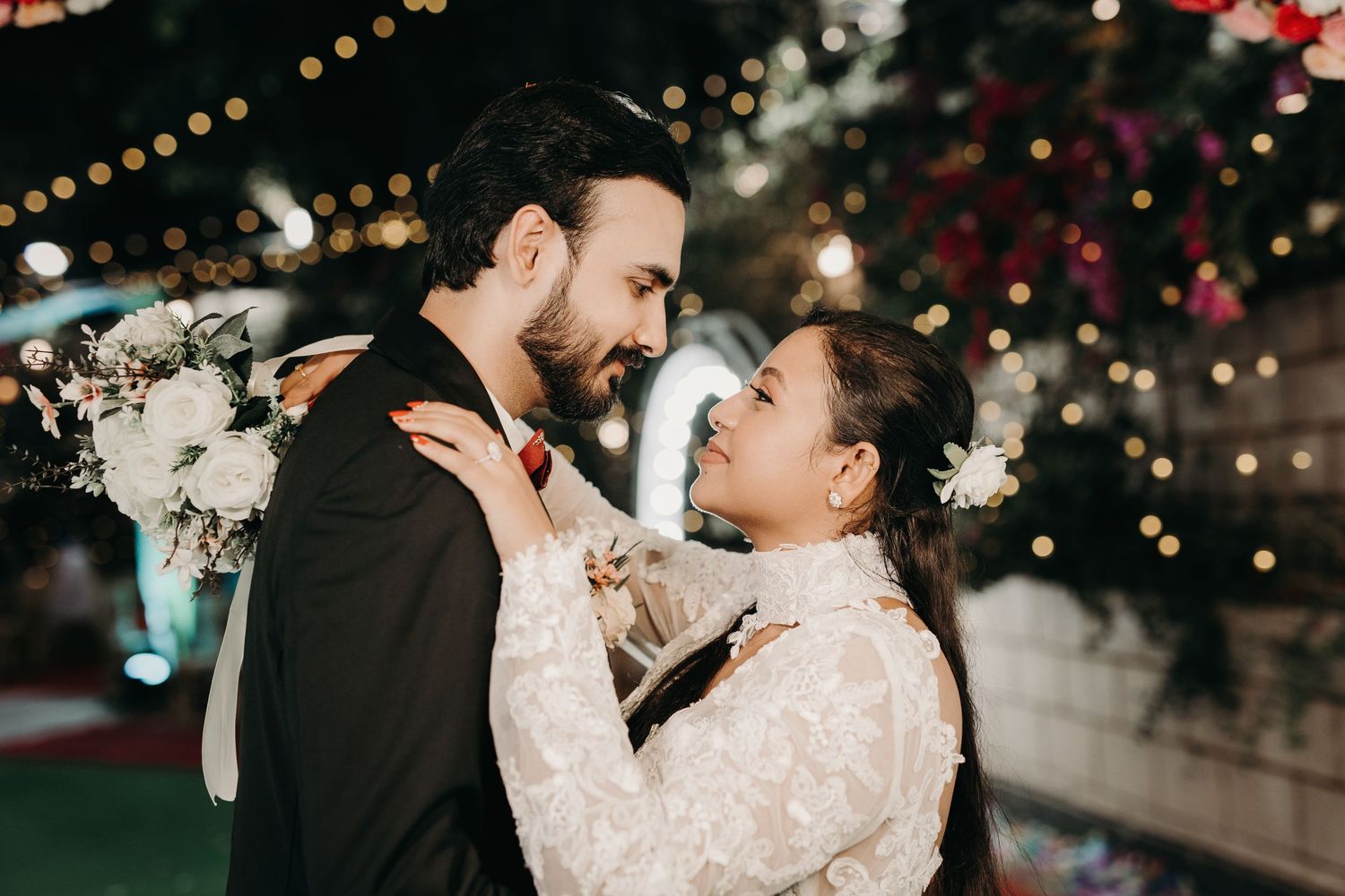 Wedding couple sharing tender moments under twinkling lights and floral arrangements.