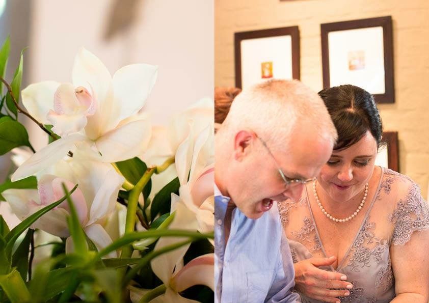 White orchid flowers with green leaves beside an elderly couple sharing a tender moment at a wedding reception.