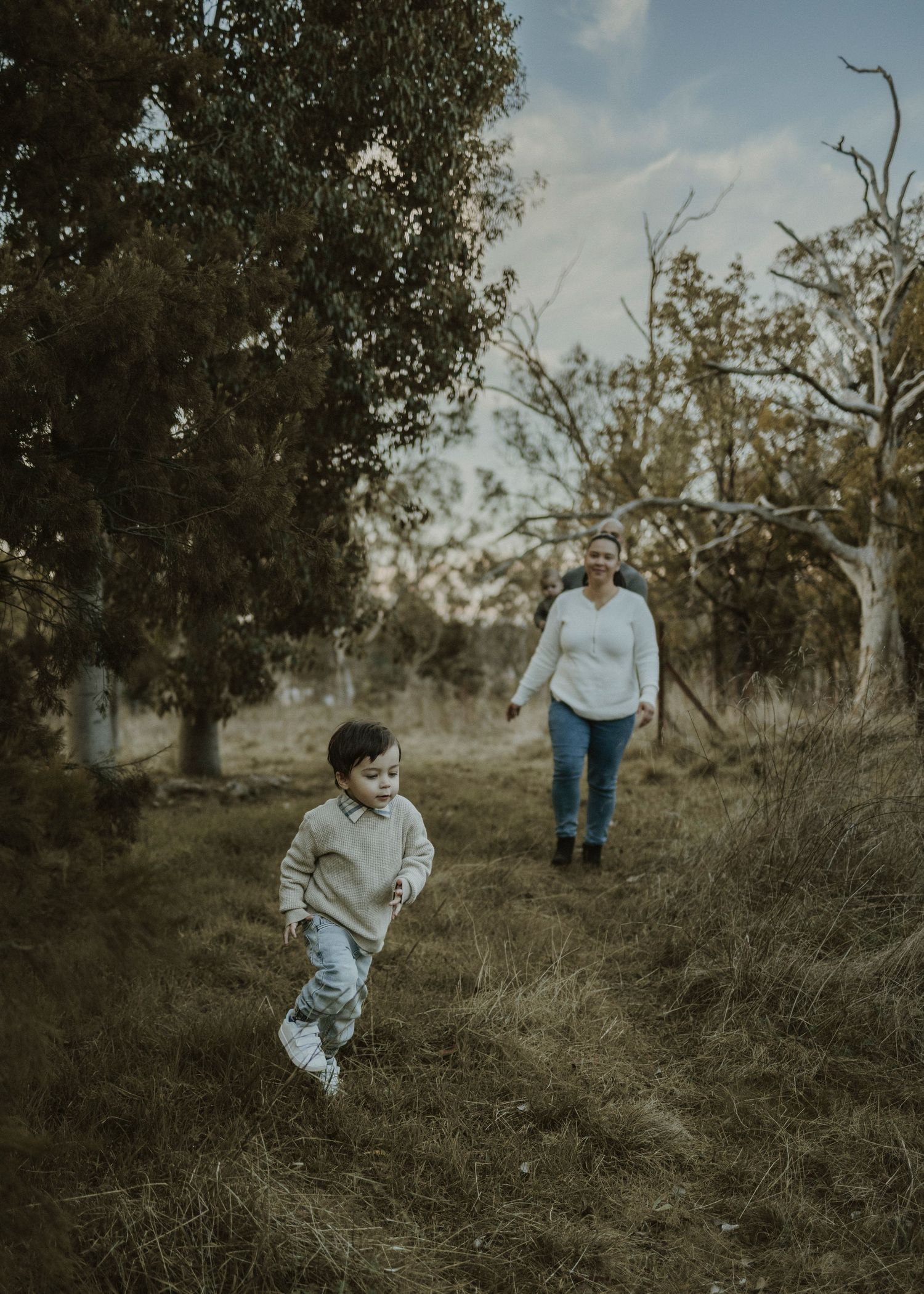 Little boy running through the nature walking track with his parents following