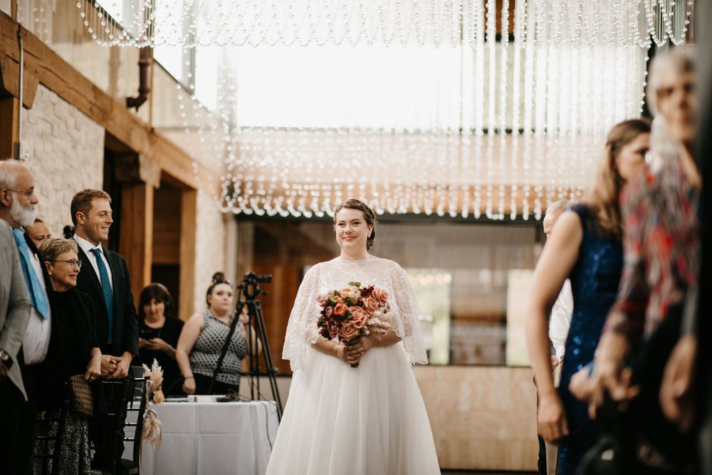 Smiling bride walking down the aisle in a white gown holding a colorful bouquet.