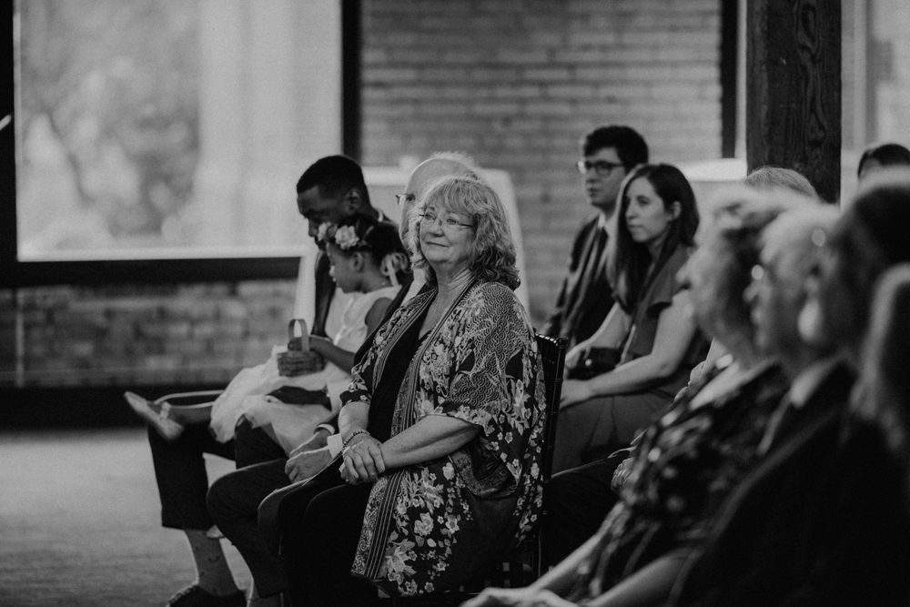 Black and white photo of wedding guests seated in rows, smiling and watching a ceremony unfold.