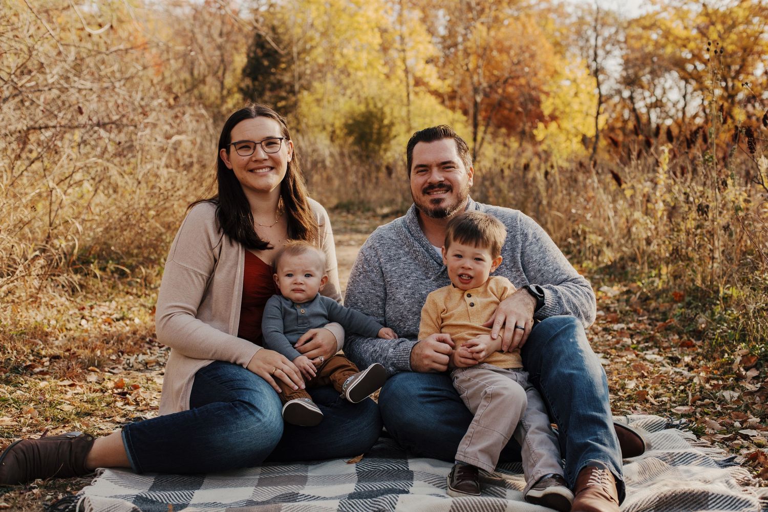 Family of four sitting together on blanket during autumn outdoor photo session.