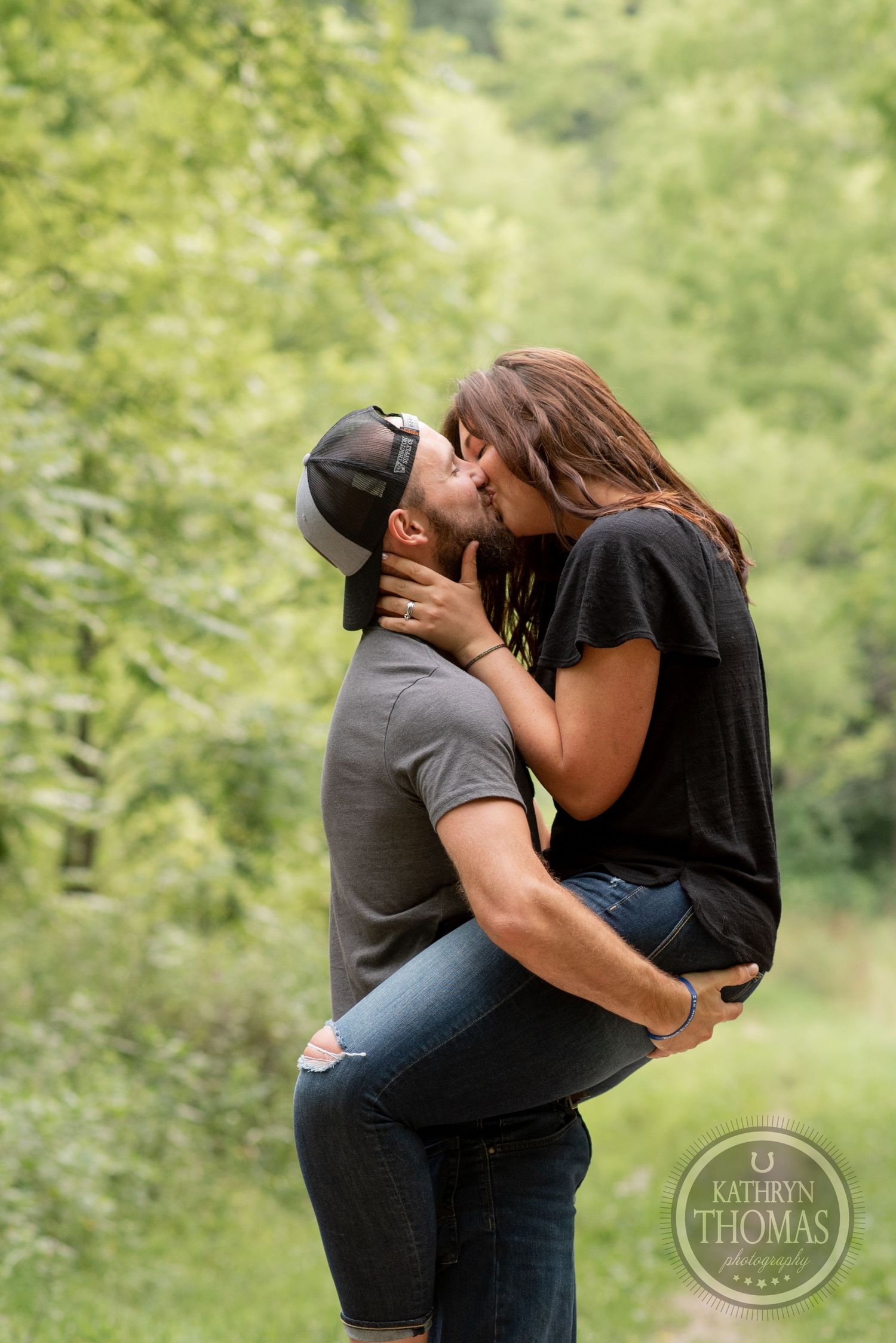 A couple sharing an intimate moment on a wooded path with bright green foliage.