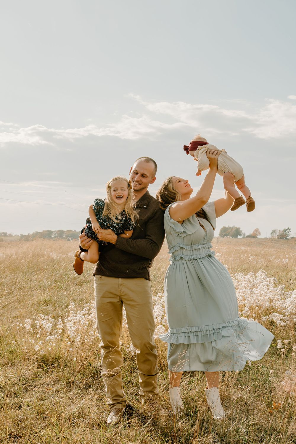 Family of four laughing and smiling together in an open field, capturing a joyful, carefree moment of love and connection.