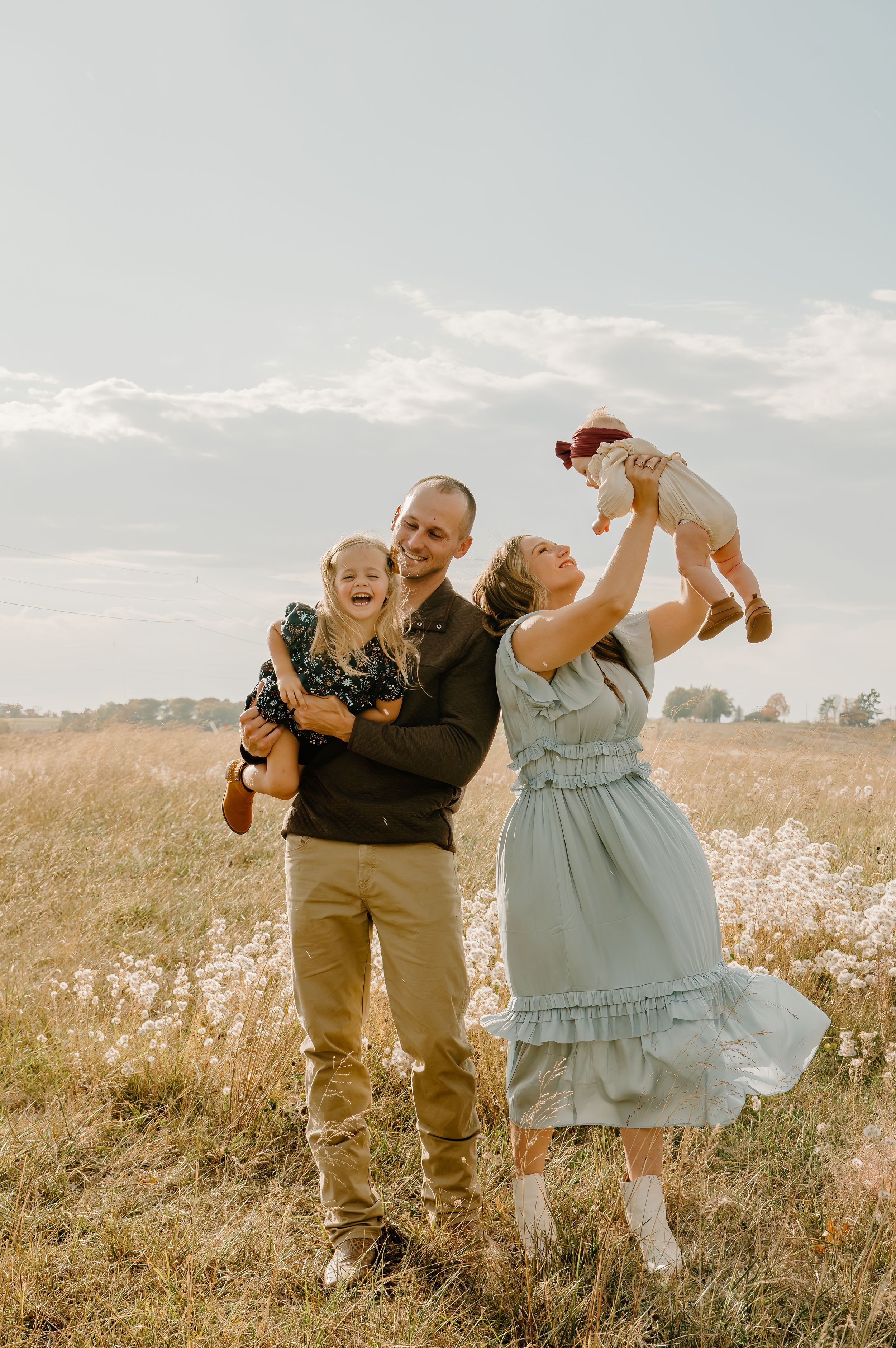 Family of four laughing and smiling together in an open field, capturing a joyful, carefree moment of love and connection.