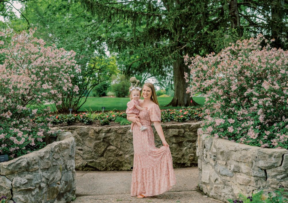 Mom & daughter sharing a sweet moment in a public garden, surrounded by blooming roses, capturing the beauty of their bond