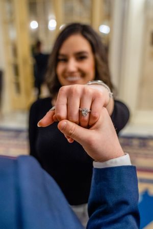 Close-up of hands displaying an engagement ring in an ornate building interior.
