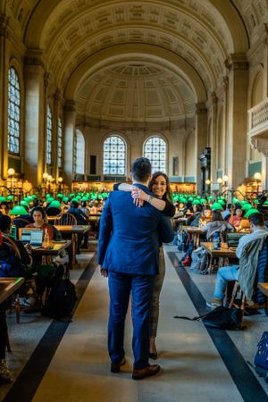 A romantic moment in a grand library hall filled with study tables and green lamps.