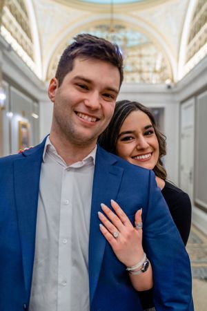 A newly engaged couple showing off the ring in an elegant hallway with domed ceiling.