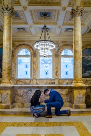A special moment unfolds beneath a crystal chandelier in a grand marble-columned room.