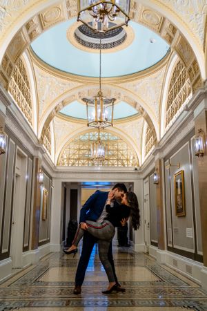 A dramatic dance dip pose in an elegant corridor with domed ceilings and marble floors.