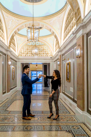 Two people conversing in an ornate hallway with marble floors, decorative ceiling and hanging chandeliers. Copley Square Hotel in Boston, MA