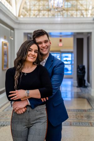 A happy couple embracing in an ornate hallway with classical architecture and decorative floors.