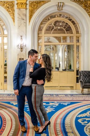 A romantic embrace on an ornate patterned carpet in a luxurious gold-trimmed hallway.