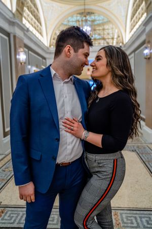 A romantic moment shared in an elegant corridor with decorative ceiling and classical architecture.
