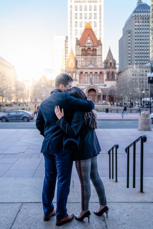 A couple embraces outside Trinity Church in Boston's historic Copley Square at sunset.