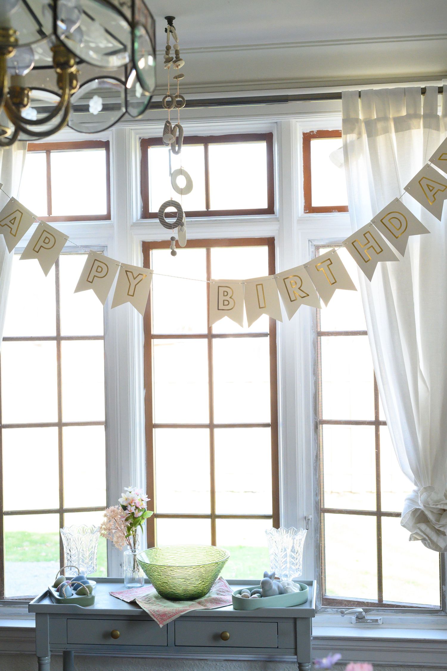 Happy Birthday banner hanging in bright window with vintage table and party decor.