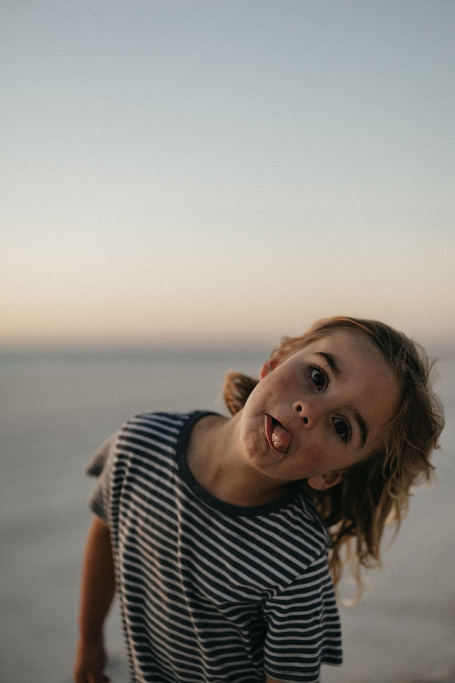 Child making playful expression at beach during golden hour.