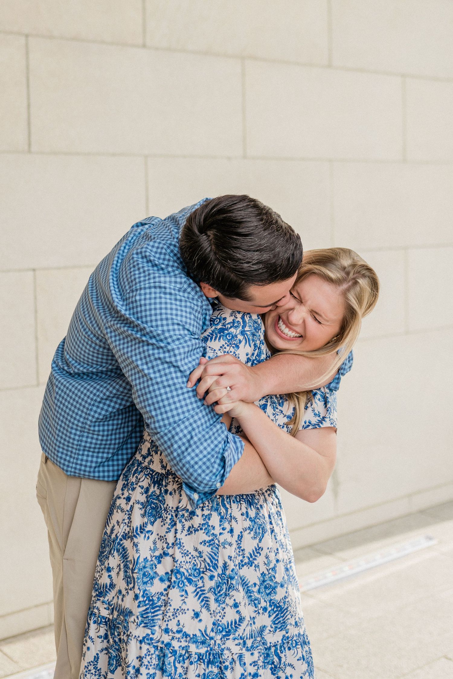 A joyful couple shares a candid laughing moment against a white brick wall.