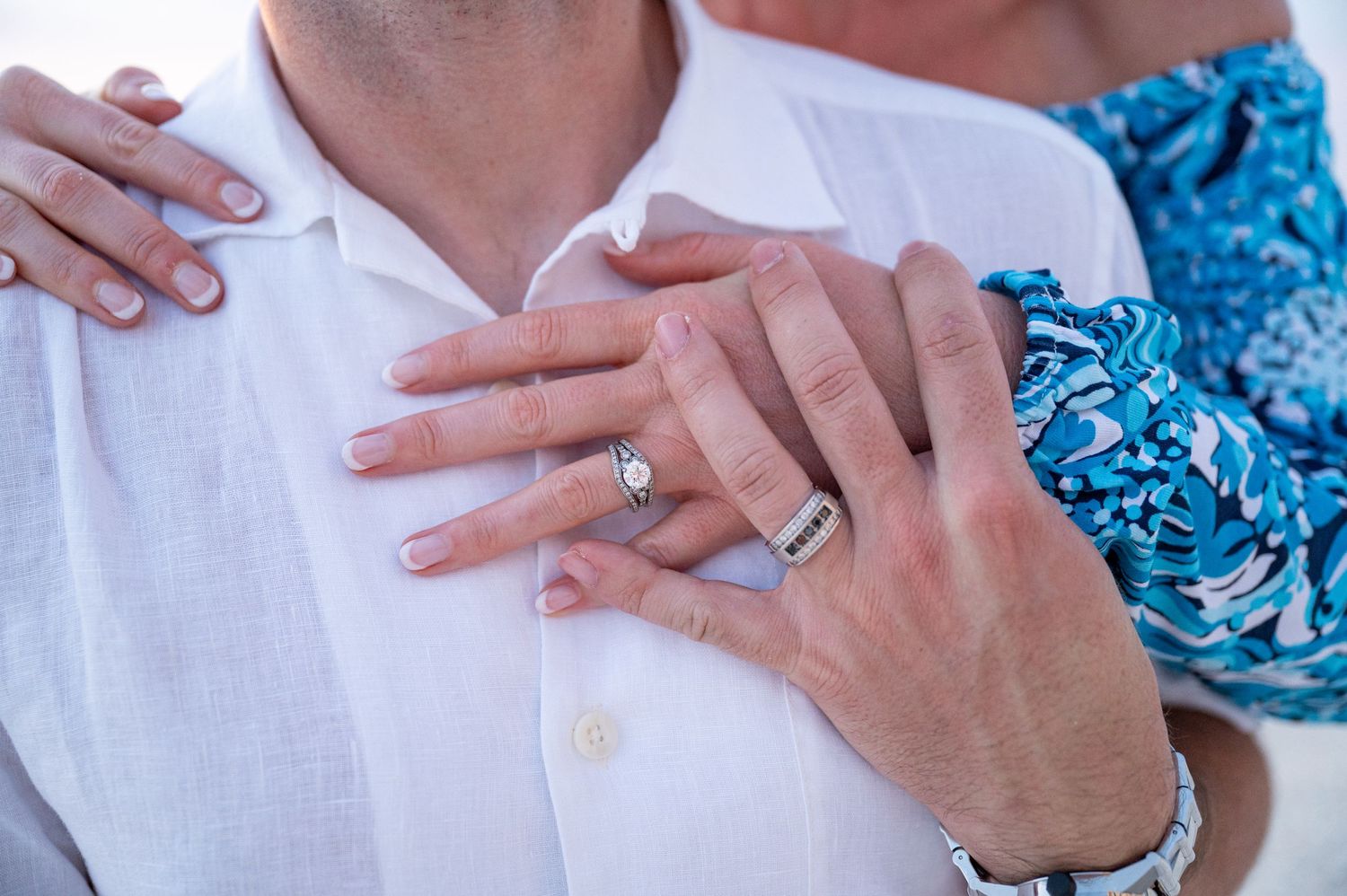 Close-up of hands showing wedding rings against white shirt.