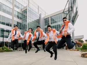 Group of graduates in academic regalia jumping in celebration outside modern university building.