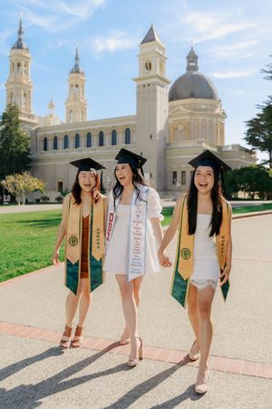 College graduates in cap and gowns pose on campus with a beautiful domed church building in the background.