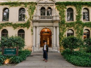 Graduate stands in archway of ivy-covered historic university building entrance.