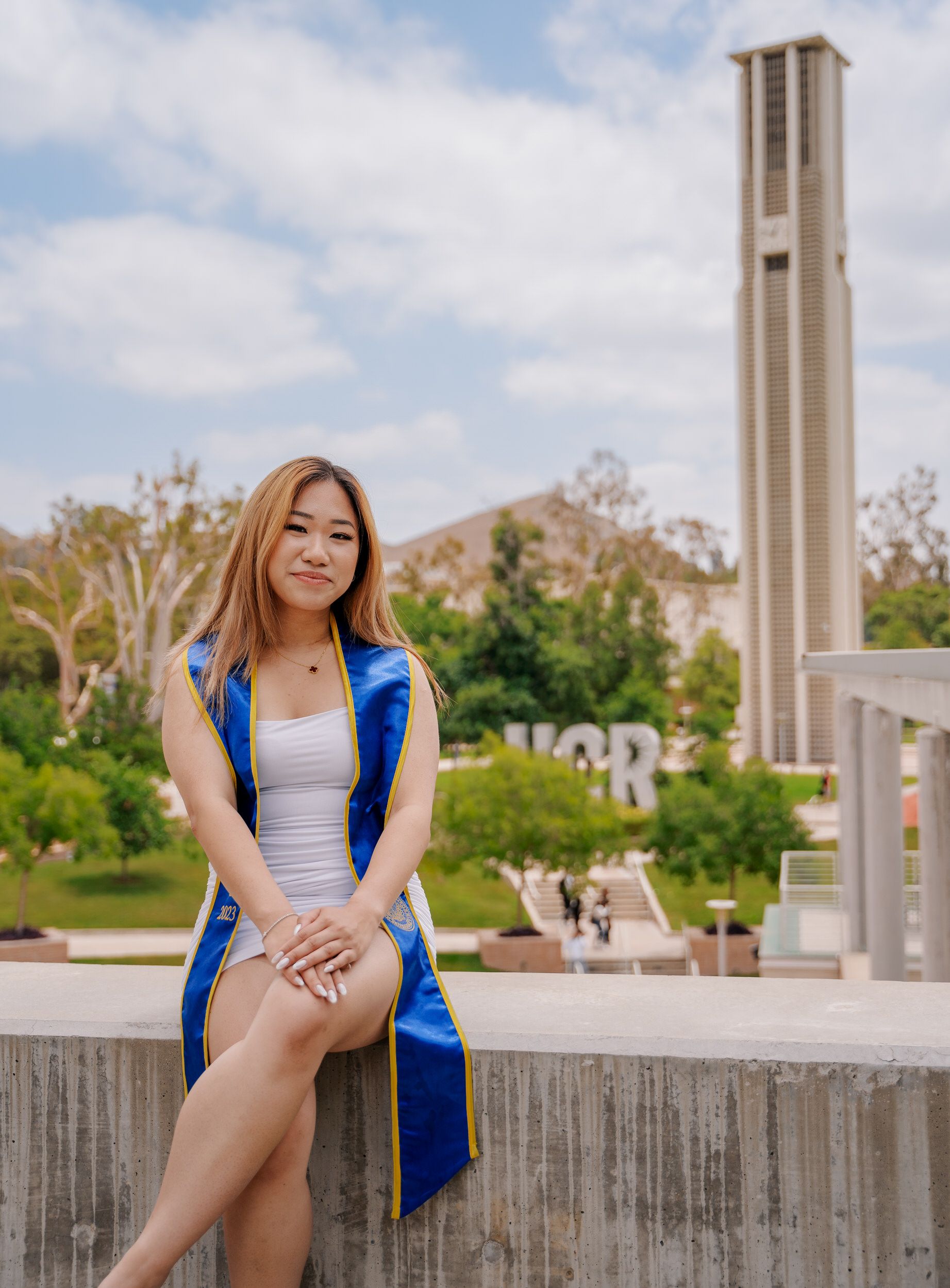 Graduate in blue graduation stole poses near campus bell tower.