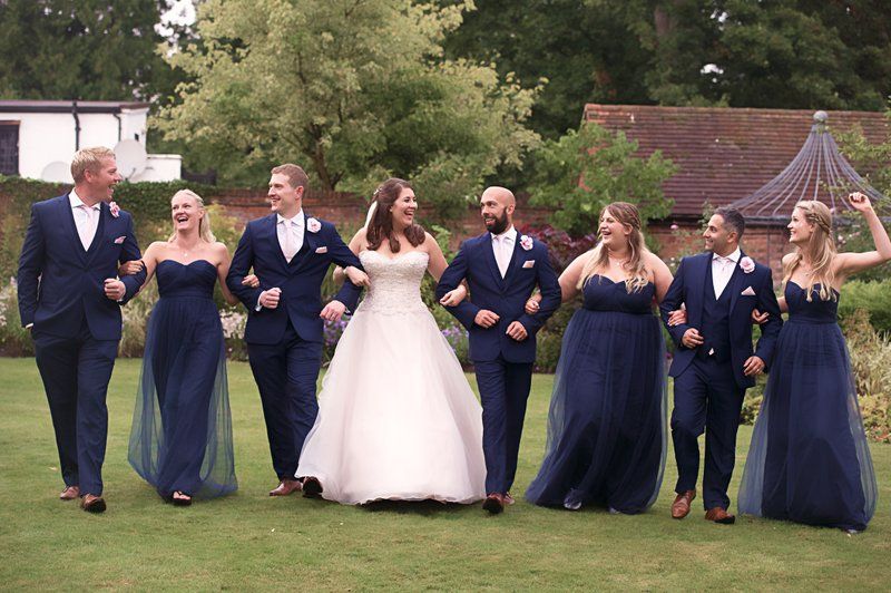 Wedding party in navy blue and white formal attire walks together on green lawn.