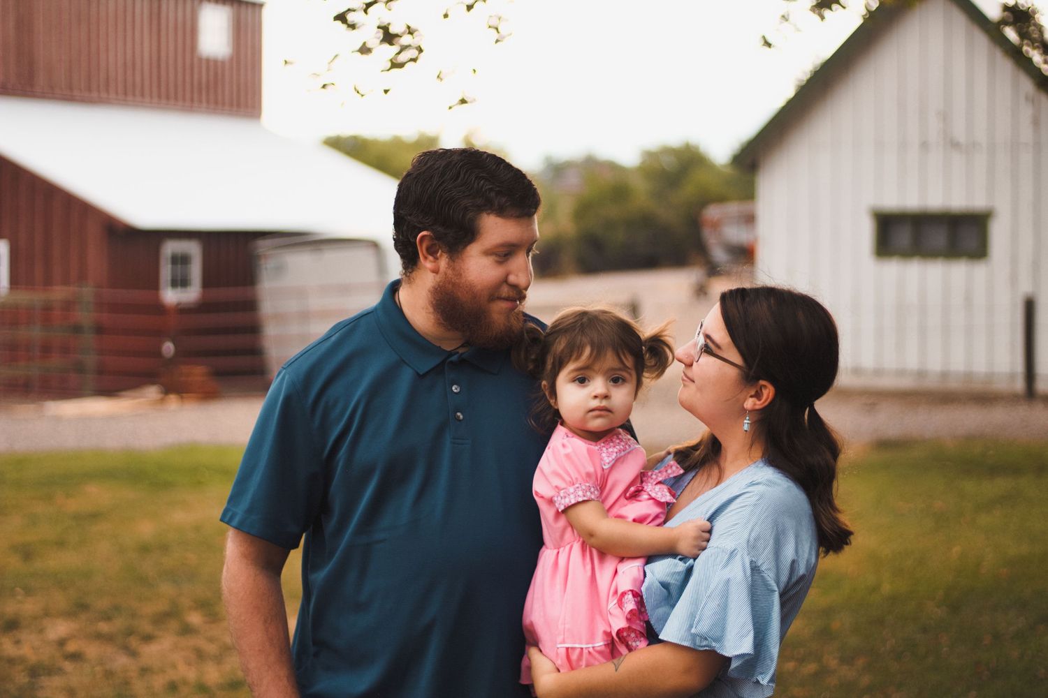 proud parents looking at each other holding toddler baby girl barn rustic setting