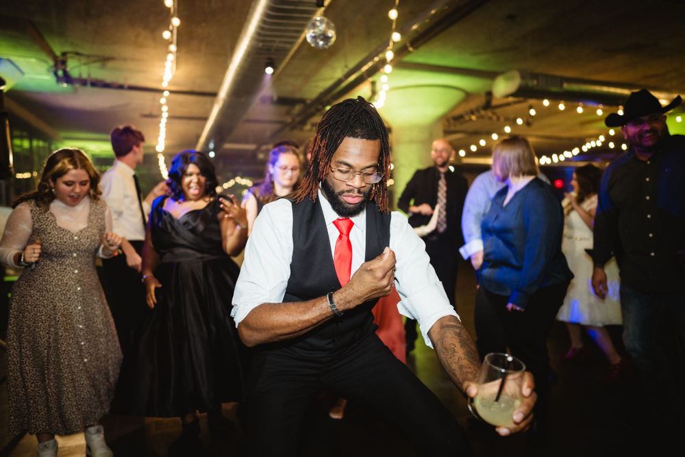 A dancer in a white vest and red tie shows off energetic moves on a crowded dance floor.