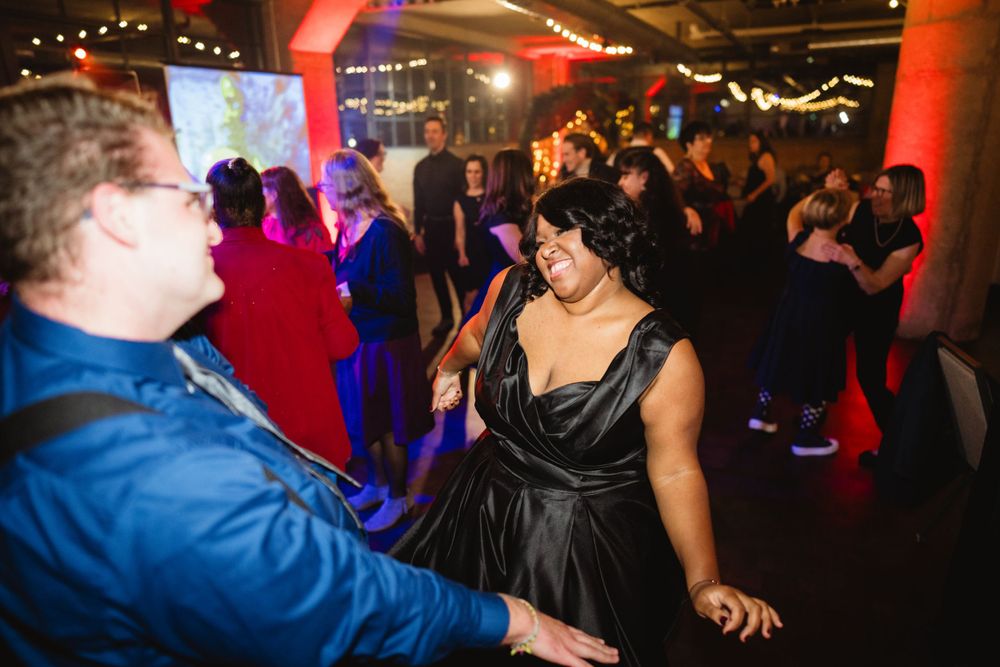 Wedding reception guests dancing under colorful lights and exposed industrial ceiling.