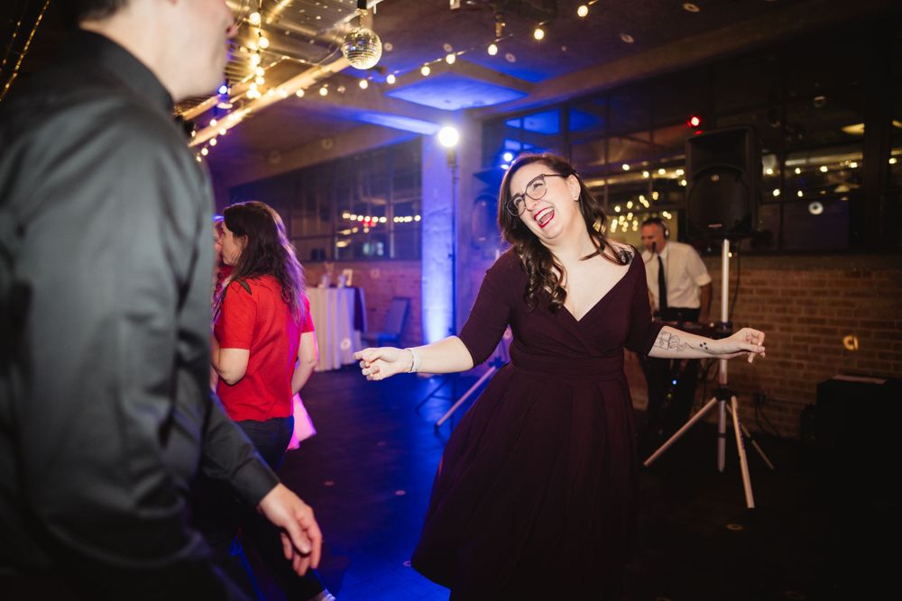 A person in a burgundy dress dances enthusiastically at an indoor party with blue lighting.