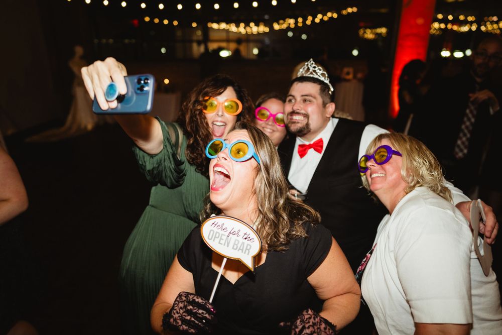 Party guests taking selfies and posing with props at a festive indoor celebration.