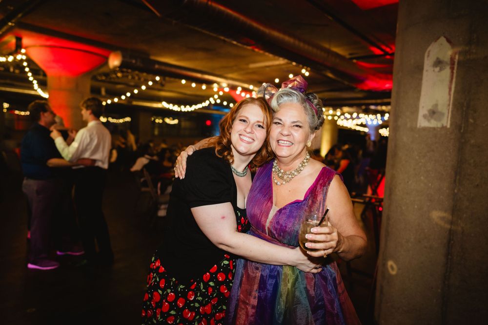 Two people dancing together at a celebration with colorful lighting and festive atmosphere.