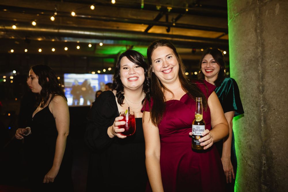 Party guests enjoying drinks and smiling at a festive indoor event with string lights and green accents.