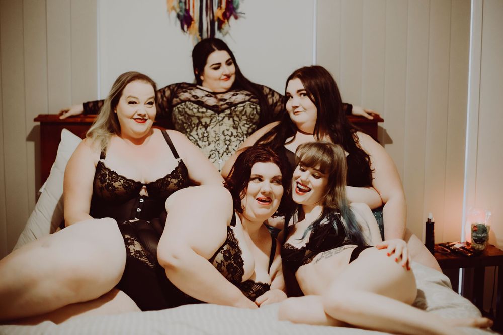 group of women in lingerie posing together on bed and smiling at camera
