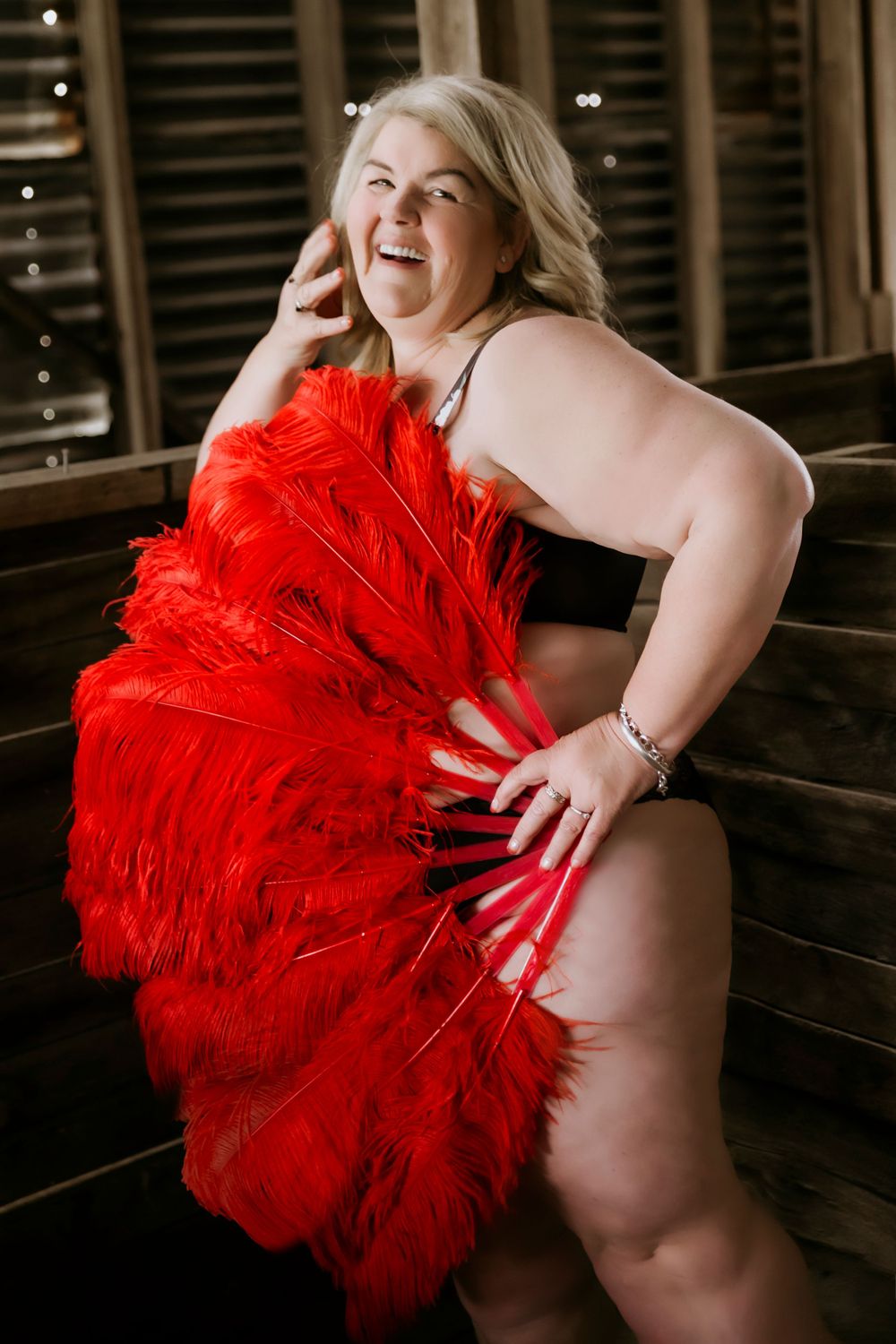 plus size mature blonde in black lingerie holding red feather burlesque fan